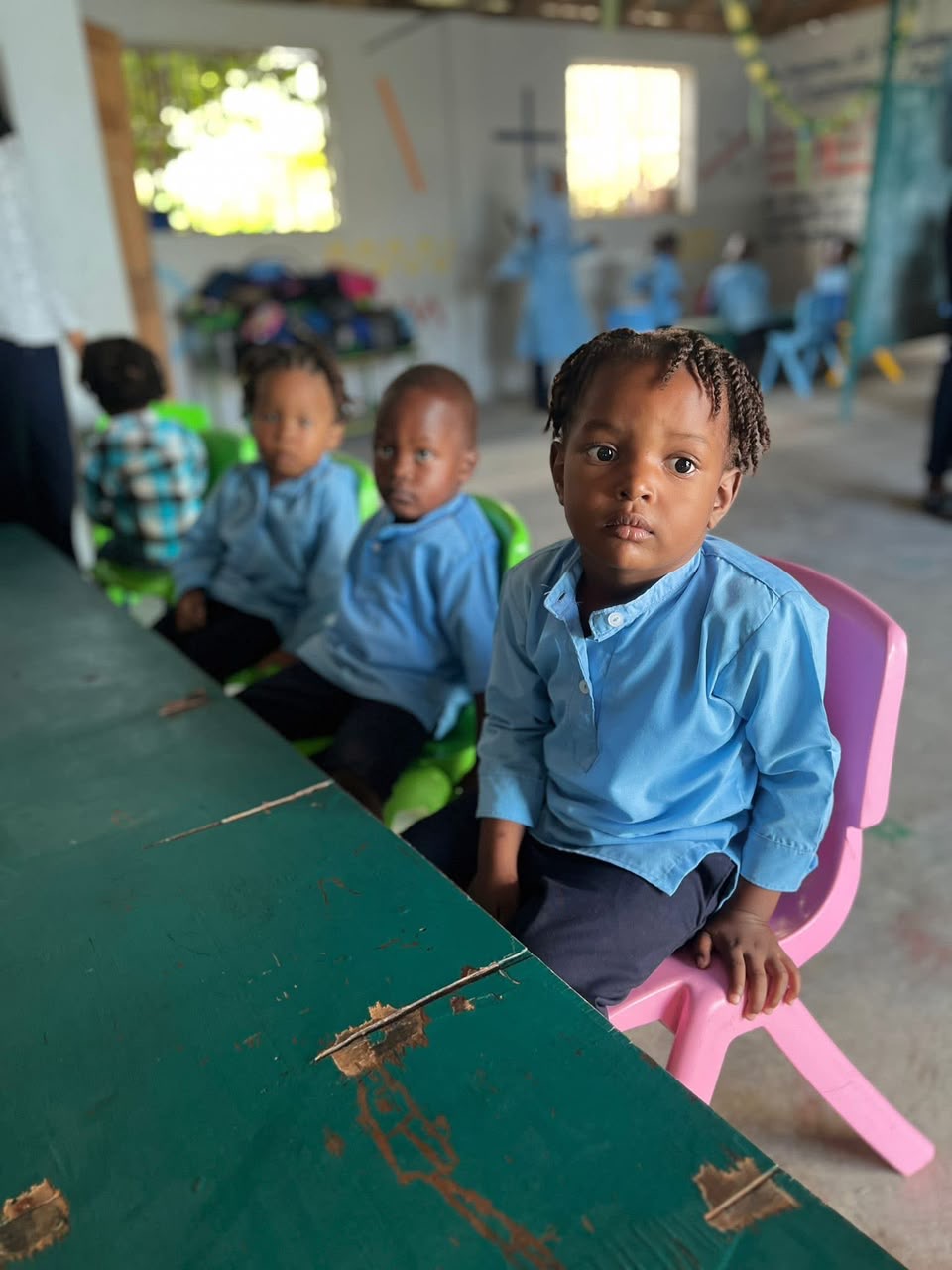 Young children in blue uniforms seated at a classroom desk at Aisha School